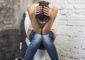 Woman Suffering From Constipation Sitting On Toilet In Restroom Indoors