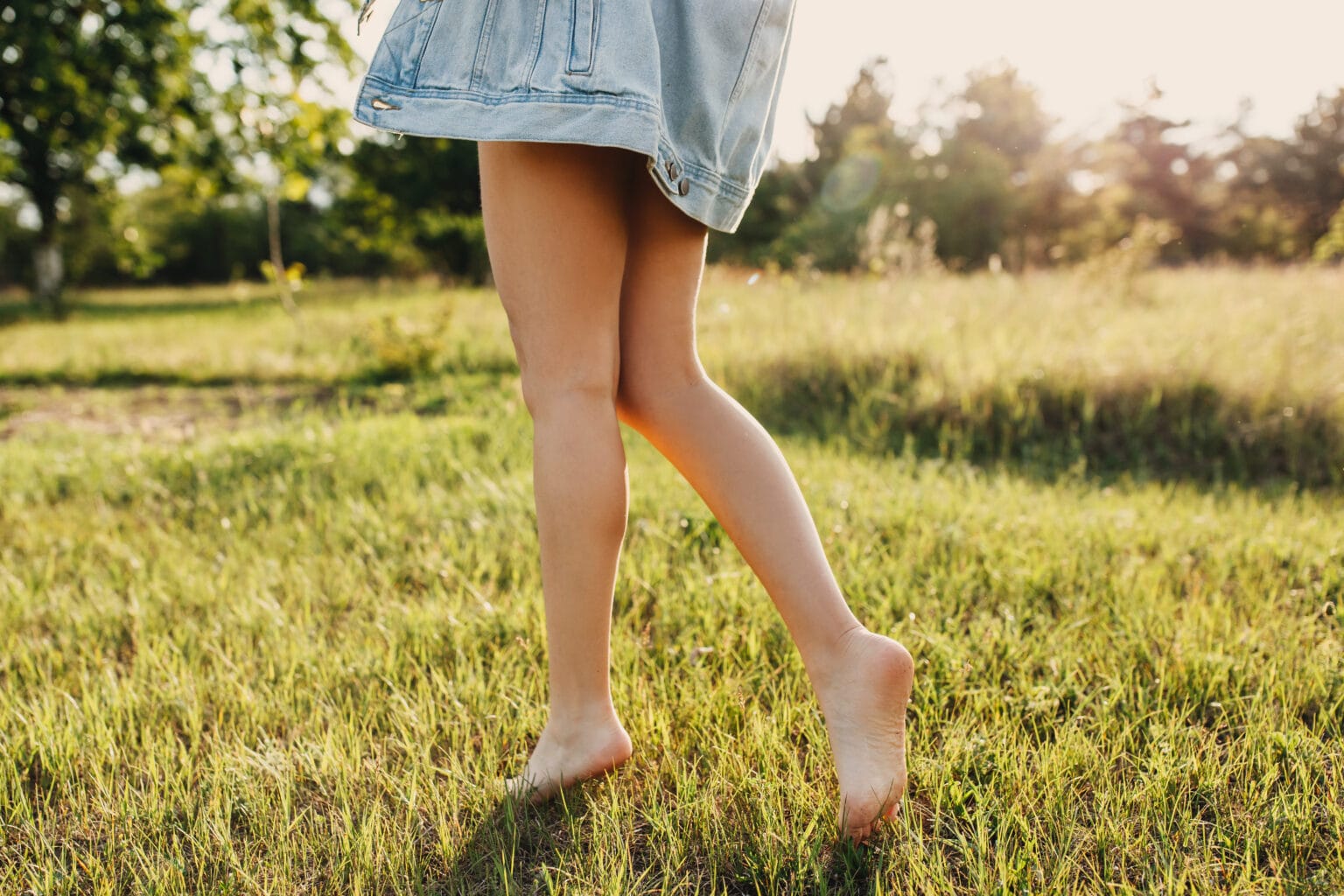 Illustrative photograph of bare lower legs walking through sunlit grass.