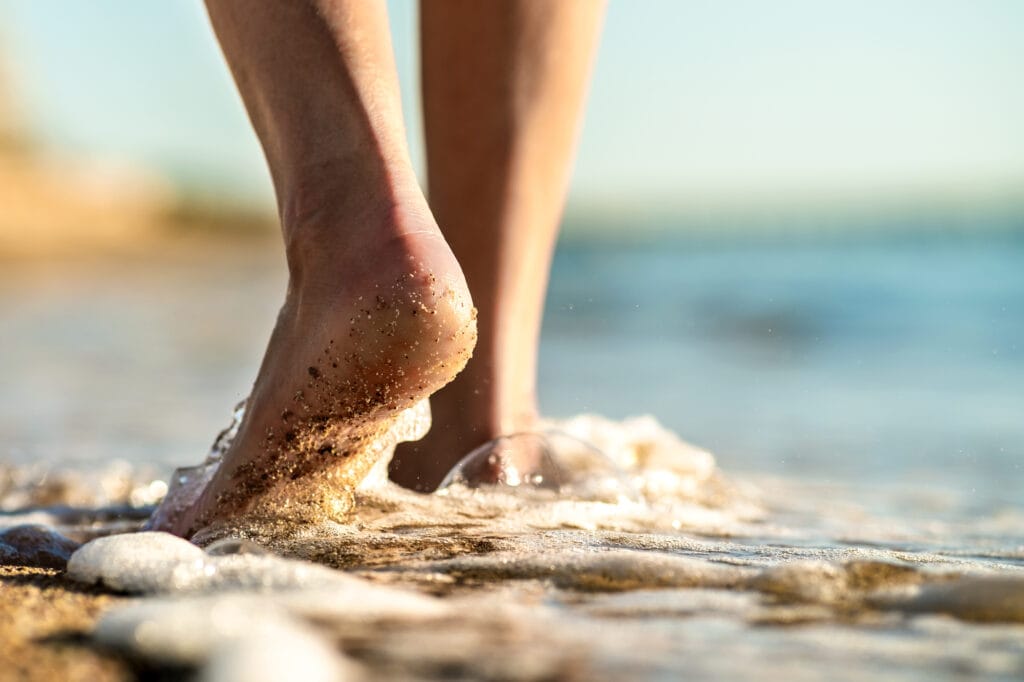 Illustrative photograph of bare ankles stepping at the edge of the sea.